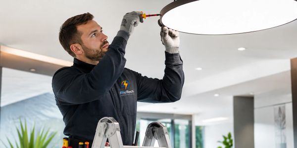 Technician fixing a ceiling light with a screwdriver indoors.