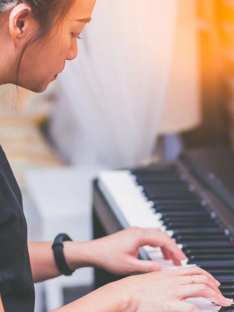 A person playing the piano with focused concentration in warm lighting.