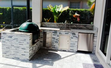 Modern outdoor kitchen with grill and dishwasher in a sunny backyard.
