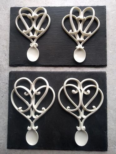Four decorative white heart-shaped spoons on black boards.