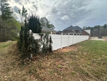 A long white fence bordering a green yard near houses under a cloudy sky.