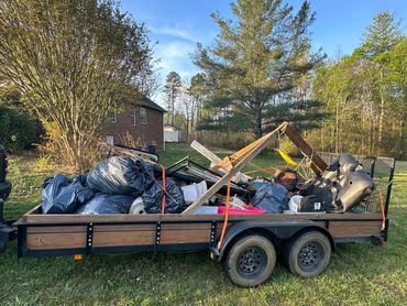 Trailer loaded with various bags, furniture, and debris in a yard.