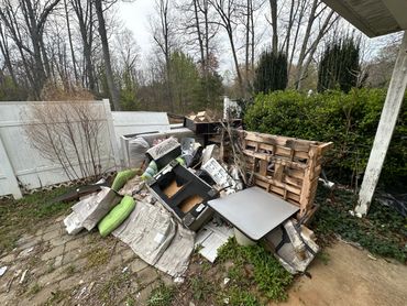 Pile of discarded household items and debris in a backyard corner.
