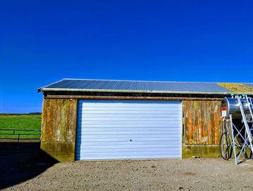 Rustic barn with solar panels on the roof under a clear blue sky.