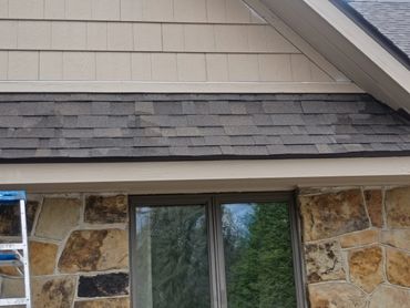 Exterior wall with stone facade, window, and roof shingles.