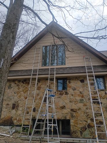 Multiple ladders set up against a stone and wood house for exterior work.