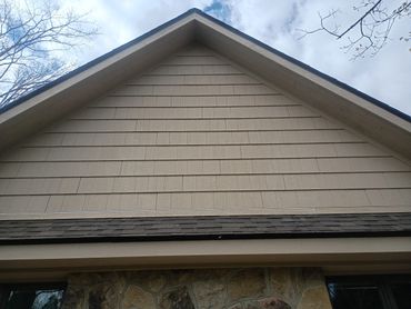 The upper exterior of a house with beige siding and a triangular roof.