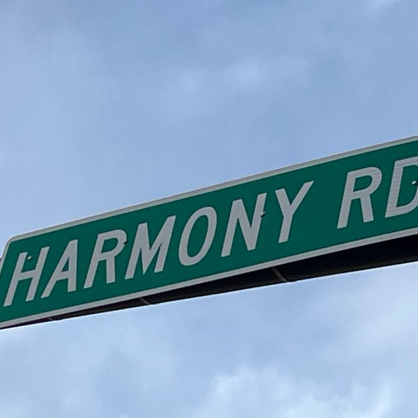 Street sign reading Harmony Rd against a cloudy sky.