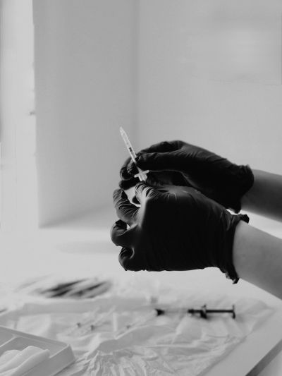 Hands in black gloves preparing a syringe for injection.