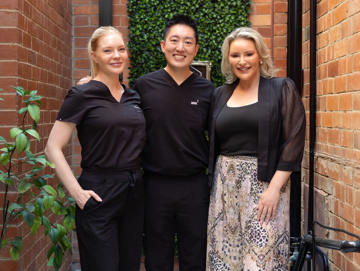 Three smiling professionals standing closely in a narrow brick alleyway.