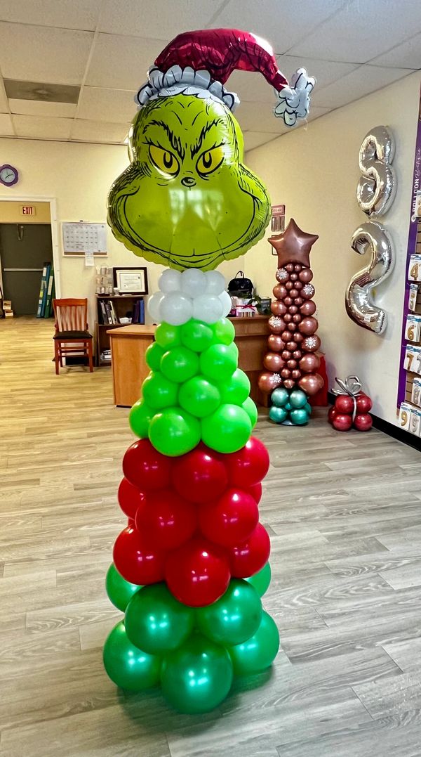 Grinch-themed Christmas balloon tower with red, green, and white balloons.