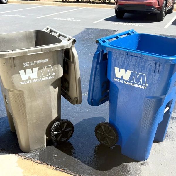 Two Waste Management bins, one gray and one blue, placed on a wet pavement.