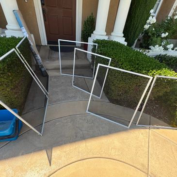 Four window screens leaning against a hedge near a front door.