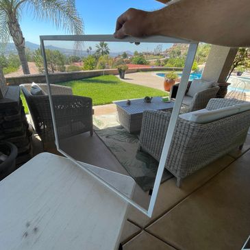 Hand holding a transparent window screen with a backyard view.