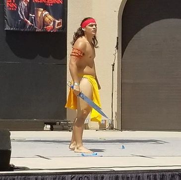 Man dressed in traditional warrior attire holding a sword on stage.