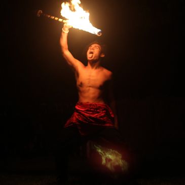 A man performing a fire dance with a torch at night.