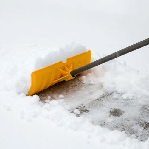 A yellow snow shovel pushing snow off a paved surface.