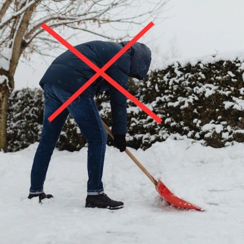 A person slouched over a snow shovel, illustrating poor body mechanics while removing snow. 