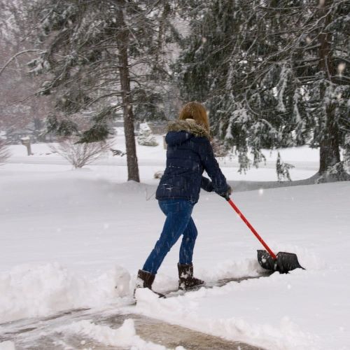 A woman using proper mechanics while pushing snow off a driveway.