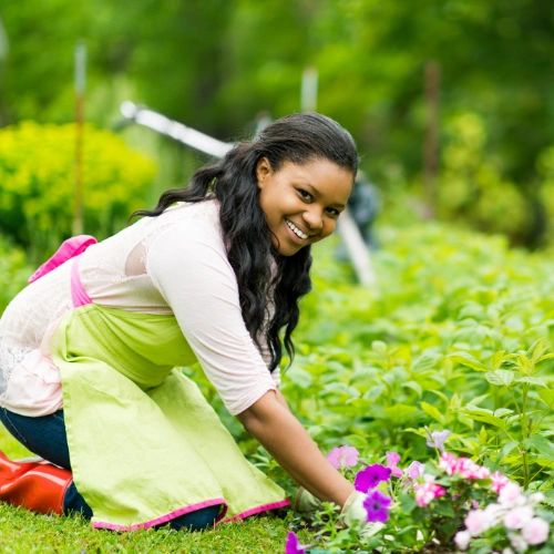 A woman kneeling on the grass and tending to her garden.