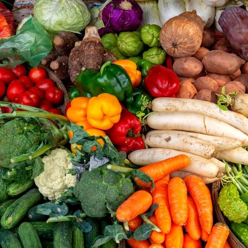 Close up of seasonal veggies, including broccoli, peppers, carrots, potatoes, cucumbers, and tomatoes