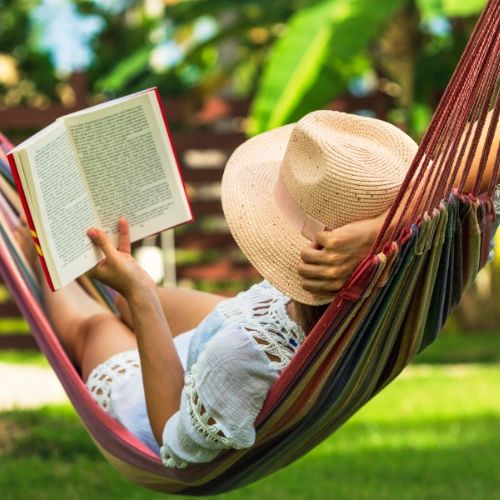 A person lying in a hammock reading a book.