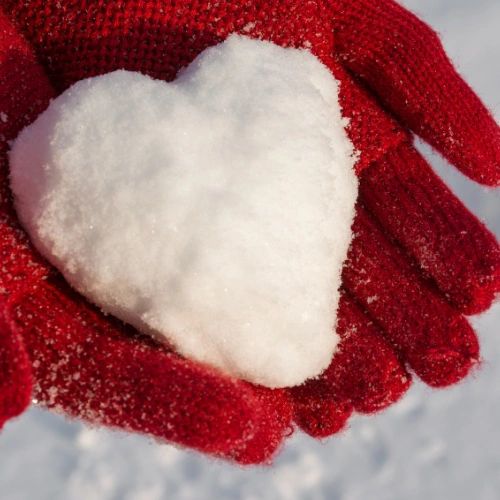 Hands wearing red winter gloves holding snow in the shape of a heartrtt