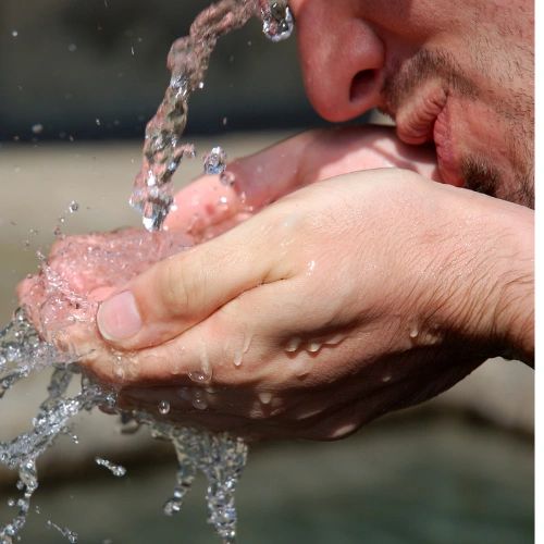 Zoomed in photo of a person drinking water from a water fountain that they have scooped in their hands