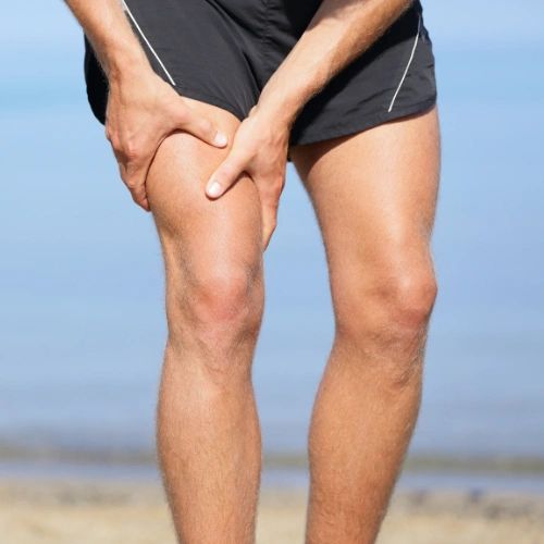 A zoomed in photo of a person holding their thy that is cramping while at the beach