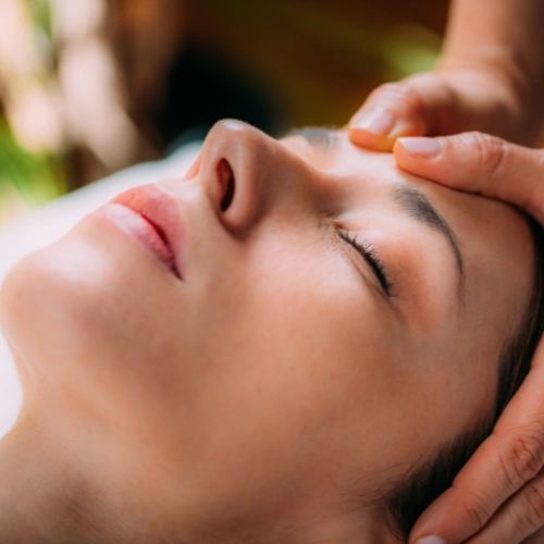 Client lying on massage table with massage therapist working on their temples