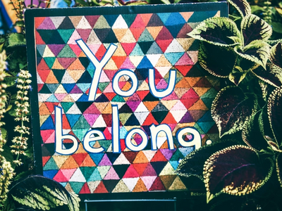 A colourful  square mosaic set amidst plants, reading the words "You belong."