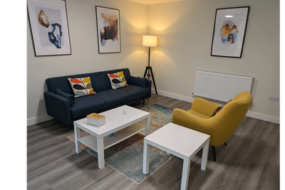 Ilkley Therapy room with a grey sofa, yellow armchair, floor lamp and small  white coffee tables. 