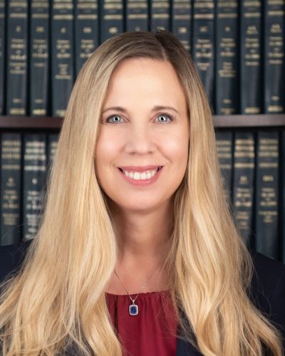 Smiling woman with long blonde hair in front of bookshelves.