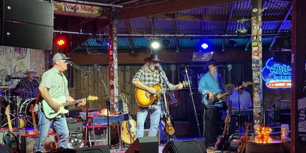 A country band performs live on a rustic stage with guitars and drums.