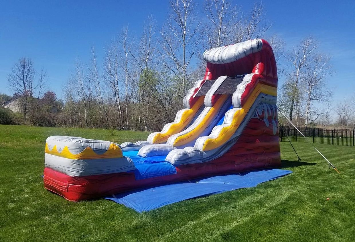 A colorful inflatable water slide set up on a green lawn under a clear blue sky.