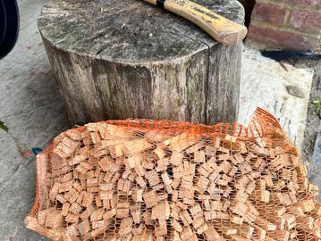 A hatchet on a chopping block with a netted bag of kindling wood.