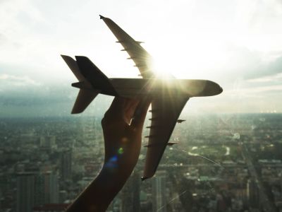 Hand holds a toy airplane against a city skyline.