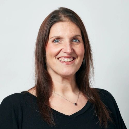Smiling woman with long brown hair and blue eyes against a plain background.