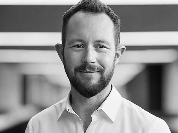 Black and white portrait of Max smiling with short hair and a beard wearing a light collared shirt.