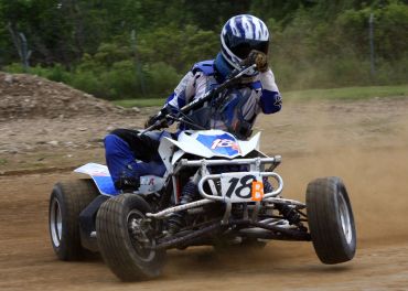 Racer on a blue quad bike speeding on a dirt track.