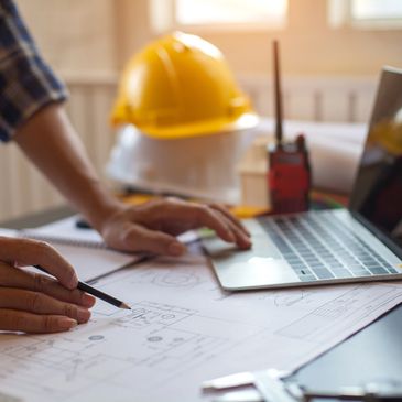 Men's hands with a computer, pencil and hard hat