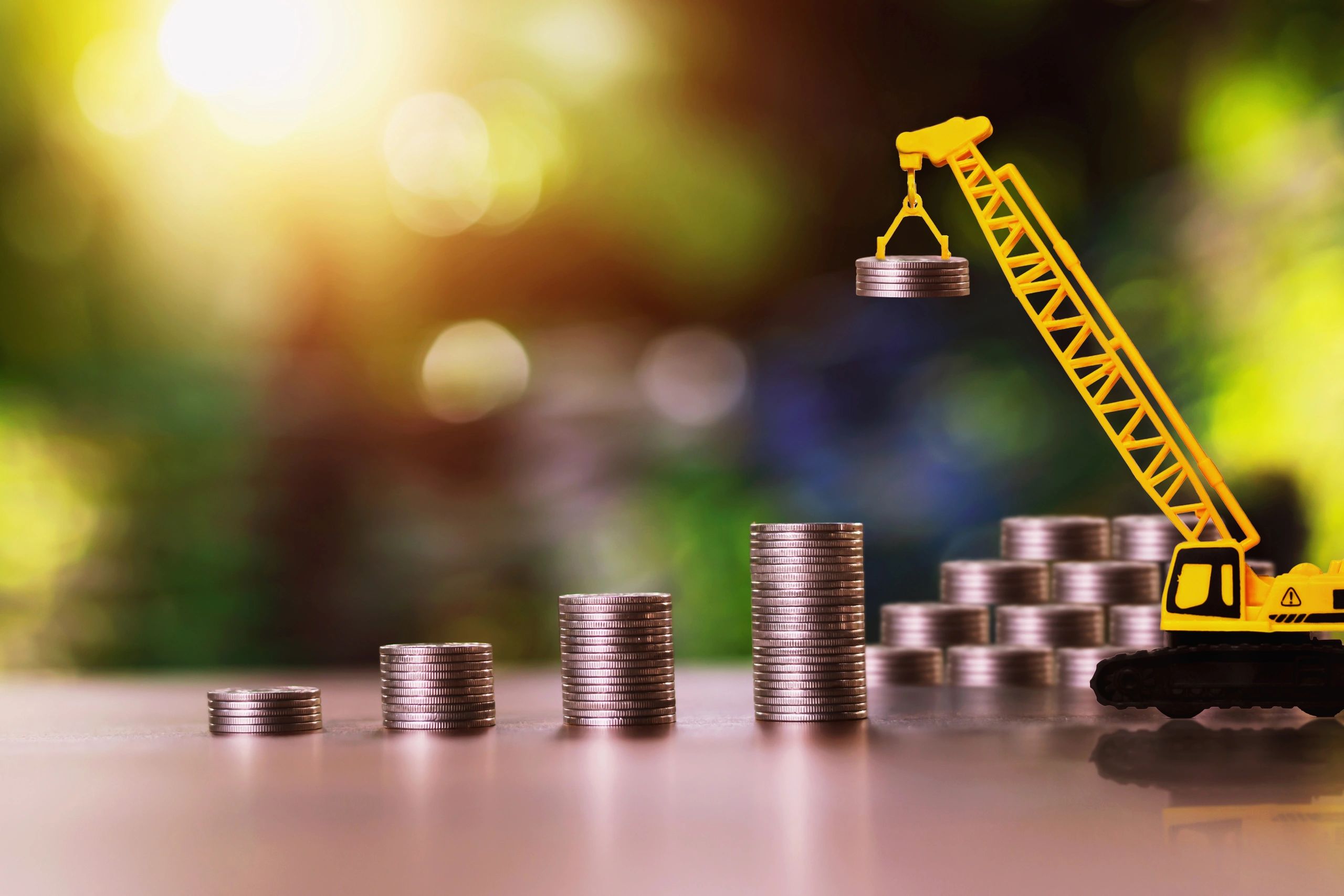 A toy-sized crane holding a stack of coins in the foreground with many stacks of coins in the rear