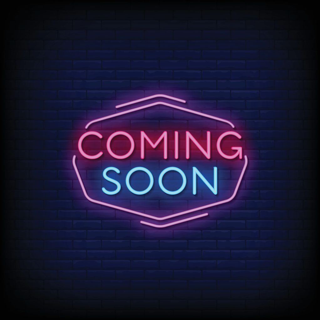 Neon sign with 'Coming Soon' text glowing against a dark brick wall.