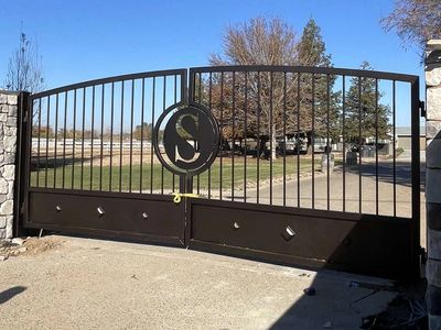 Black metal gate with an 'S' emblem under clear blue sky.