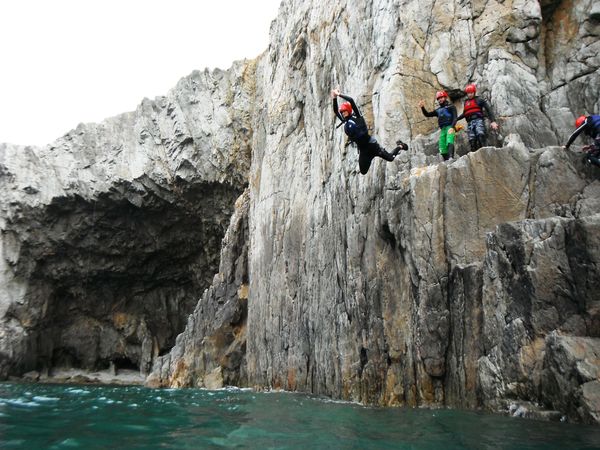 A person jumping off rocks into the sea below while coasteering.