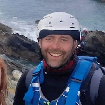 6 people wearing coasteering equipment taking a selfie with the coastline in the background