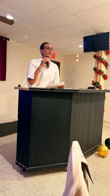 Woman speaking at a podium with microphone in decorated room.