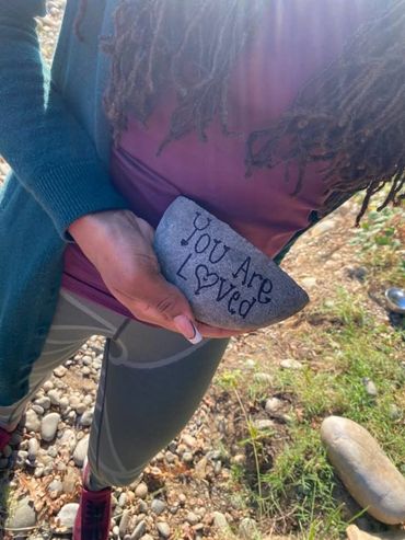 Person holding rock with 'You Are Loved' written on it outdoors.