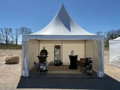 Outdoor white event tent with a person inside and a refrigerator.