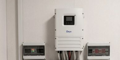 A white Deye device mounted on a wall with electrical panels on either side.